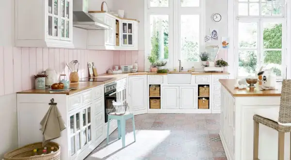 Une cuisine campagne chic lumineuse avec des meubles blancs, un plan de travail en bois, un carrelage coloré et de grandes fenêtres donnant sur le jardin.