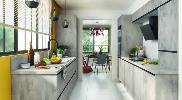 Cuisine moderne avec des meubles gris béton, une cuisine en parallèle fonctionnelle et un espace repas lumineux visible à travers une arche.