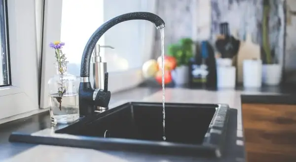 Un robinet noir verse de l'eau dans un évier, suggérant la filtration eau du robinet pour une boisson pure et saine.