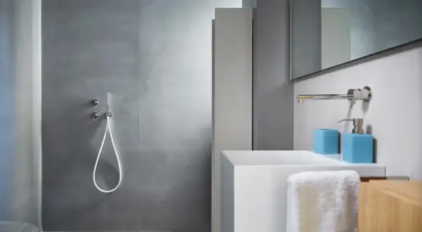 Salle de bain moderne avec douche sans carrelage, lavabo blanc et accessoires bleus.