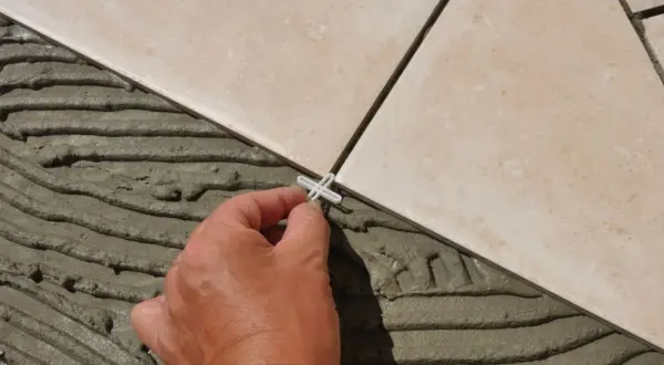 Pose de carrelage en cours, une main place un croisillon. Le prix pose carrelage m2 dépend de la complexité.