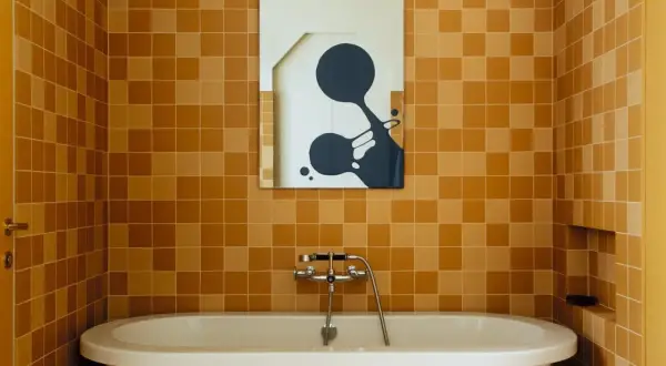 Salle de bain aux tendances carrelage ocre, baignoire blanche et miroir abstrait.