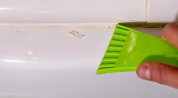 Main verte utilisée pour enlever joint silicone sale sur une surface blanche.