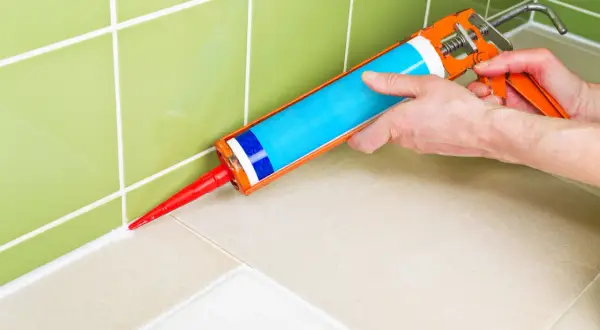 Application d'un nouveau joint blanc avec un pistolet à silicone pour refaire le joint de douche.