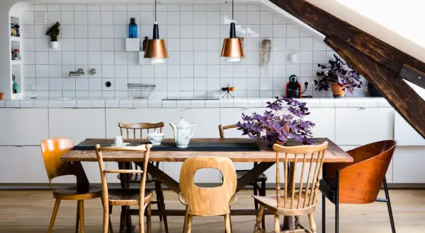 Une cuisine ouverte en L avec un îlot central en bois, des chaises vintage et des suspensions cuivrées. Une plante violette apporte une touche de couleur.