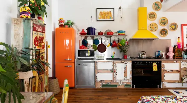 Cuisine colorée avec frigo orange vif, vaisselle suspendue et une astuce rangement cuisine : des portes de placard dépareillées pleines de charme.