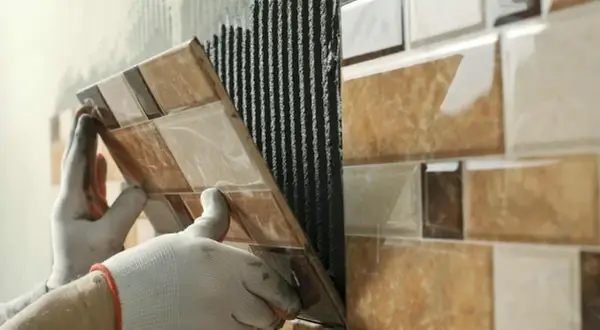 Pose de carrelage sur carrelage, une main gantée appliquant une nouvelle rangée sur le mur déjà carrelé.