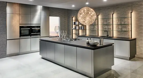 Une cuisine chic et moderne aux finitions métalliques, avec un îlot central, des fours intégrés et des étagères lumineuses.