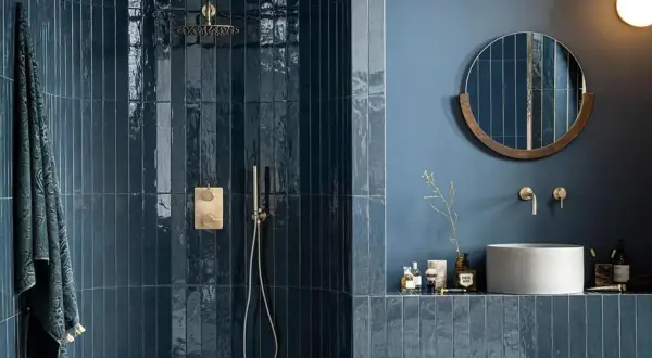Élégante salle de bain bleu nuit avec douche à l'italienne carrelée, miroir rond en bois et vasque en béton.