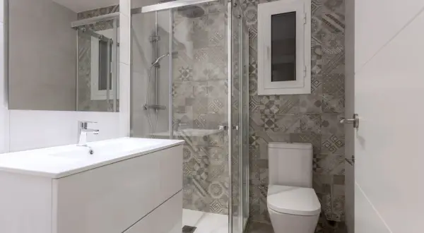Salle de bain petite aux tons gris. Carrelage mural à motifs géométriques, douche vitrée, lavabo blanc et WC.