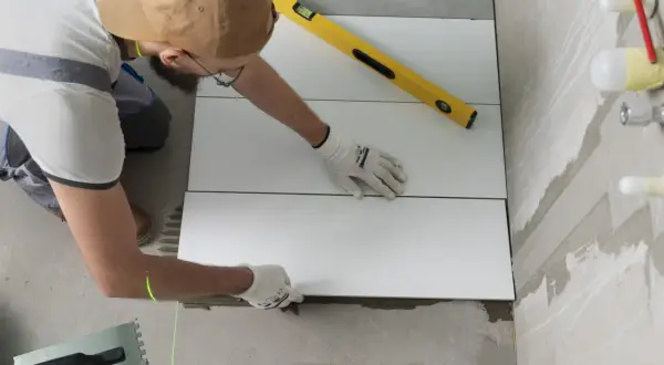 Pose d'un carrelage mural de salle de bain. Un carreleur utilise un niveau et un laser pour un calcul précis.