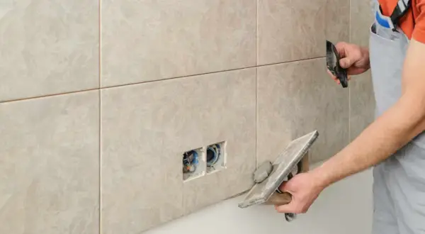 Un carreleur applique un joint époxy sur des carreaux muraux. Il utilise une taloche pour étaler le mortier.