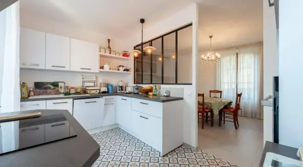 Carrelage décoratif au sol pour la délimitation carrelage cuisine salon. Une cuisine moderne blanche ouverte sur une salle à manger avec lustre.
