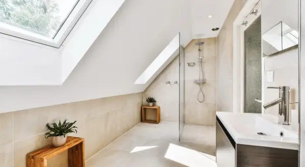 Salle de bain sous pente avec douche à faible hauteur, lavabo moderne et puits de lumière.