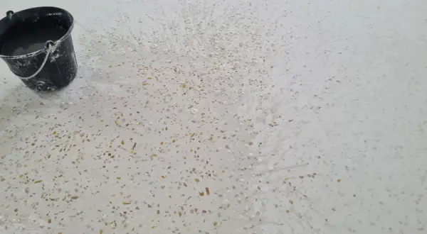 Un seau d'eau éclabousse un sol en terrazzo blanc moucheté, révélant comment faire briller un sol en terrazzo.
