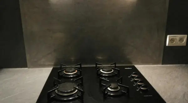 Plaque de cuisson noire avec quatre feux, devant un mur de crédence gris métallisé.
