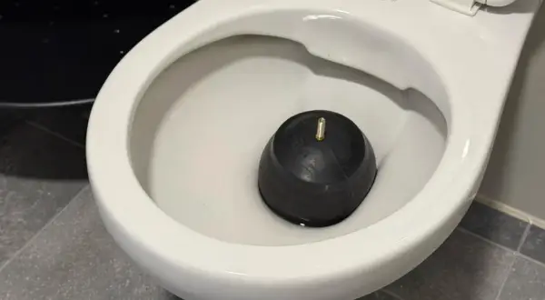 Un déboucheur en caoutchouc noir repose dans la cuvette d'un WC, prêt à résoudre les problèmes de diamètre d'évacuation WC.