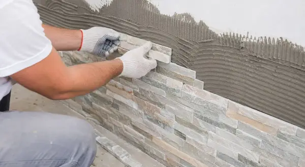 Pose de pierre de parement sur un mur avec du mortier. Un artisan pose méticuleusement les pierres pour un revêtement mural naturel.
