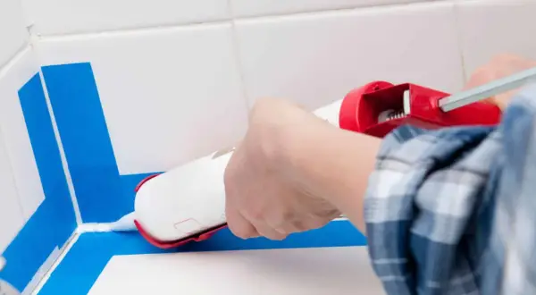 Application d'un joint silicone blanc avec un pistolet pour assurer l'étanchéité de la douche. Le bon quel joint pour douche est essentiel.