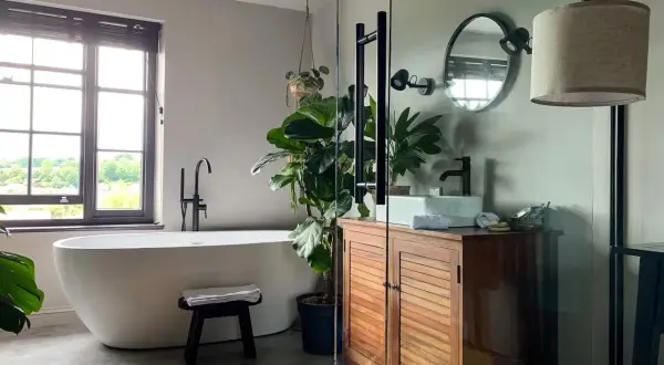 Une baignoire îlot, un meuble en bois et une plante luxuriante créent une ambiance de wet room apaisante.