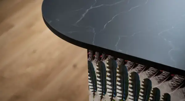 Plan de travail de cuisine en marbre noir avec un motif de plumes colorées sur le côté, créant une profondeur visuelle.
