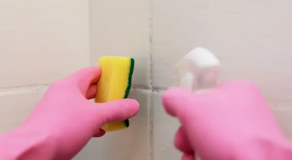 Main rose gantée tient une éponge jaune pour nettoyer une tache sur carrelage qui ne part pas.