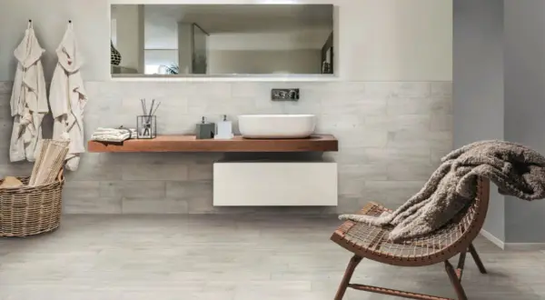 Salle de bain moderne avec murs et sol en grès cérame émaillé effet bois, lavabo suspendu, fauteuil confortable.