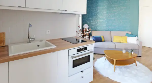 Plan d'une petite cuisine en U moderne avec évier, plaque de cuisson, four et un salon cosy avec canapé bleu et jaune.