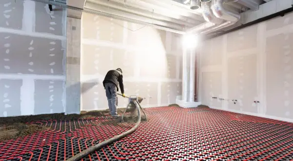 Un ouvrier installe un système de chauffage par le sol électrique, avec des tuyaux rouges sur une grille noire.