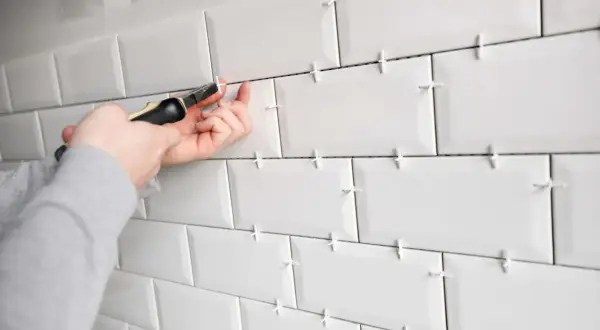 Pose de carrelage blanc avec des croisillons pour assurer un espacement parfait. Un outil est utilisé pour ajuster le **taille croisillon carrelage**.