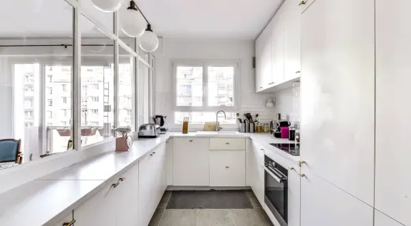 Cuisine en longueur plan, blanche et lumineuse, avec plan de travail en marbre, évier, four et rangements.