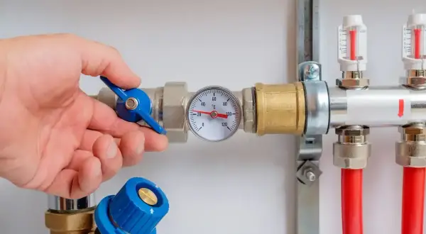 Main d'un homme ajustant la vanne d'un chauffe eau à accumulation. Un thermomètre indique la température.