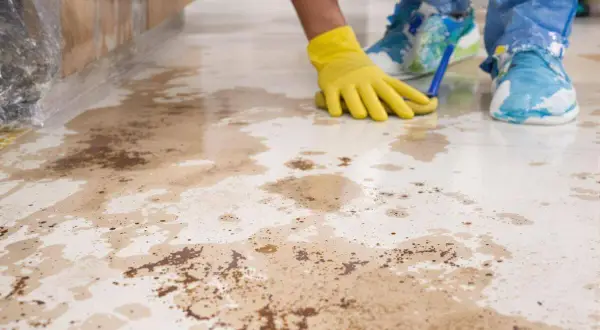 Main jaune nettoyant le carrelage taché, peut-être par de l'acide chlorhydrique.