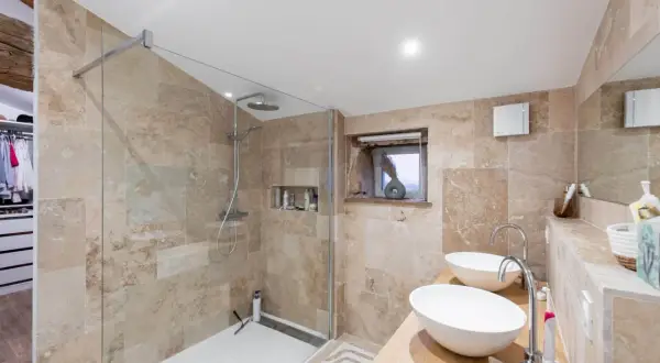 Salle de bain moderne avec douche à l'italienne, double vasque et carrelage en travertin. Une transformation réussie de rénovation salle de bain avant/après.
