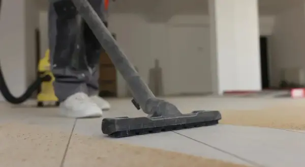 Un ouvrier utilise un aspirateur pour nettoyer le carrelage après le jointoiement. La poussière et les débris sont aspirés.