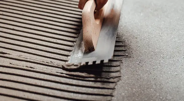 Application d'enduit pour carrelage collé avec une truelle crantée. Les sillons réguliers préparent la surface pour une pose parfaite.