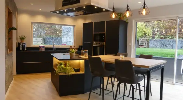 Cuisine moderne avec îlot central, plan de travail noir et carrelage marron foncé. Table haute avec tabourets, luminaire design.