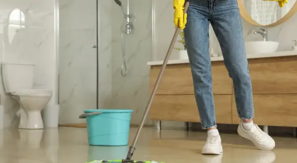 Nettoyer carrelage après chantier : une personne en gants jaunes passe la serpillière sur un sol brillant dans une salle de bain moderne.