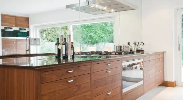 Cuisine moderne avec îlot central en bois, hotte en inox et vue sur jardin. Une belle rénovation pour une vieille cuisine.