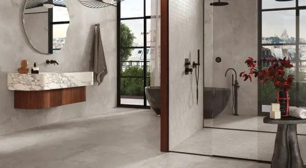 Salle de bain moderne avec baignoire îlot, douche vitrée et lavabo suspendu. La faïence grise habille les murs et le sol, créant une ambiance épurée et luxueuse.