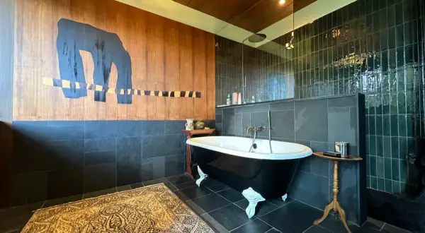 Salle de bain moderne avec baignoire sur pieds noire, tapis persan et mur boisé orné d'une œuvre d'art abstraite. Une **rénovation baignoire** réussie.