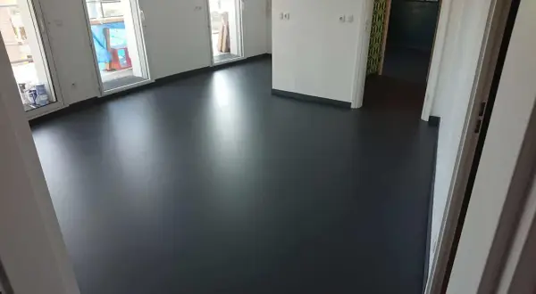 Un sol en résine époxy noir brillant, fraîchement posé, reflète la lumière dans un intérieur moderne.