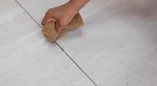 Main d'une personne nettoyant le joint carrelage avec une éponge.