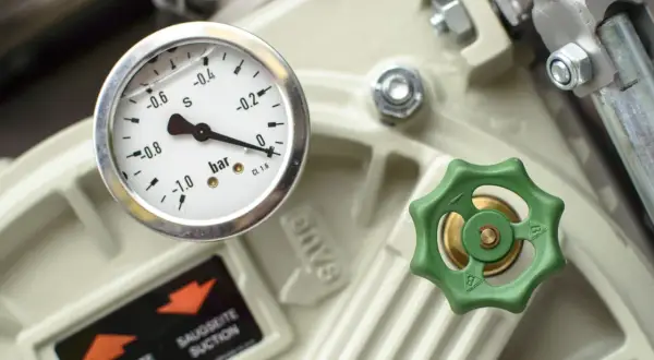Manomètre indiquant la pression sur un appareil industriel, avec une valve verte et une étiquette "SAUGSEITE SUCTION". Ce **reducteur de pression** est essentiel.
