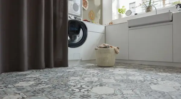 Buanderie moderne avec un sol en carrelage hexagonal aux motifs vintage. Une machine à laver et un panier à linge sont visibles.
