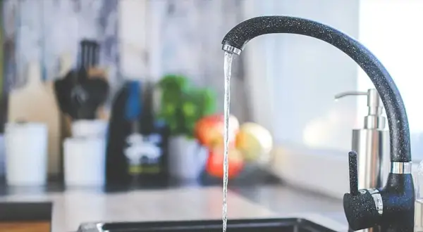 Un robinet moderne coule dans une cuisine. Un préparateur ECS discret est visible à l'arrière-plan, à côté d'un distributeur de savon.