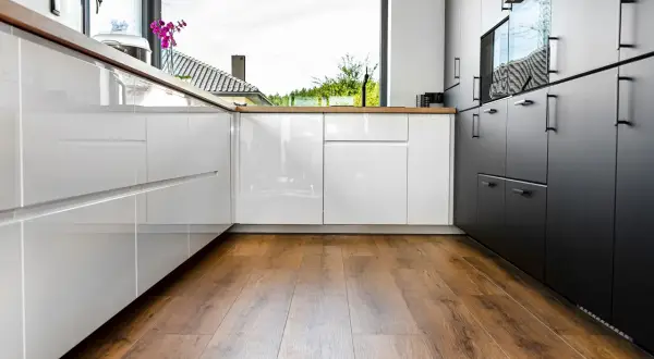 Cuisine moderne avec des armoires blanches et noires brillantes, un grand évier et un parquet au sol chaleureux.