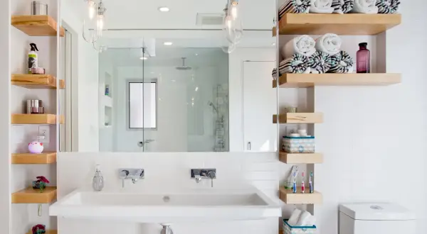 Étagères flottantes en bois pour une astuce rangement petite salle de bain. Serviettes roulées, produits de toilette et décorations y trouvent leur place.