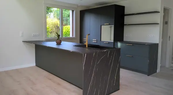 Îlot de cuisine moderne avec plan de travail en marbre noir veiné d'or. Ce modèle de cuisine simple, aux lignes épurées, est complété par des meubles sombres et un robinet doré.