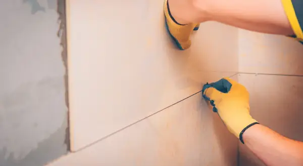Pose de carreaux : une main gantée ajuste le **taille joint carrelage** pour une finition parfaite.
